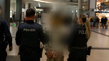 Drei Polizeibeamte laufen mit einem Festgenommenen durch die Bahnhofshalle in Nürnberg. | Bild: BR