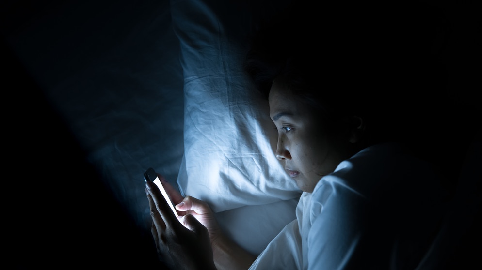 Eine Frau liegt im Dunkeln im Bett und schaut auf ihr Smartphone.
| Bild: stock.adobe.com/Kittirat