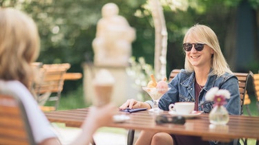 Zwei Frauen sitzen in einem Café und unterhalten sich, die eine hat einen Eisbecher und die andere einen Eiskaffee | Bild: BR/Markus Konvalin