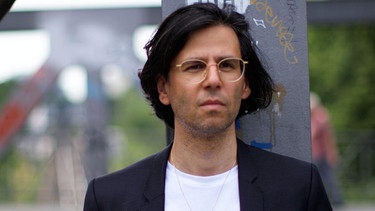 Der Autor Deniz Utlu (schwarze Haare, schlichte Brille) auf der Straße. | Bild: BR