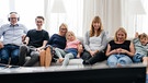 Eine Familie sitzt auf dem Sofa und schaut gemeinsam Fernsehen. Ein Familienmitglied hört die Originalsprache zur laufenden Sendung über Kopfhörer. | Bild: BR/Julia Müller