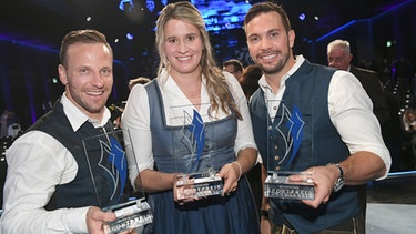 22.10.2022, Bayern, München: Die Rennrodlerin Natalie Geisenberger (M) und die Rodler die Rodler Tobias Arlt (l) und Tobias Wendl (r) stehen nach der Verleihung des Bayerischen Sportpreises 2022 mit ihrem Preis in der BMW Welt mit ihren Preisen auf der Bühne. | Bild: BSP-Regio-@dpa-Felix Hörhager