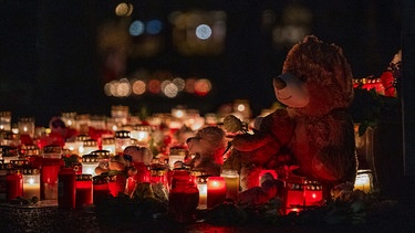 Ein Teddybär steht zusammen mit zahlreichen Kerzen auf dem Boden und erinnert an den tödlichen Messerangriff. Zahlreiche Kerzen und Kuscheltiere erinnern am Freitagmorgen im Park Schöntal an die Opfer der tödlichen Messerattacke. | Bild: picture alliance/dpa | Daniel Vogl