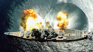 Vogelperspektive auf das Kriegsschiff USS IOWA, das während einer Übung in den Gewässern vor Vieques alle seine 15 Kanonen abfeuert. | Bild: BR/NARA gemeinfrei/PHAN Elliott