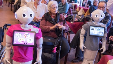 Die Roboter "Peppa" und "Pepper" stehen inmitten der Bewohner eines Alten- und Pflegeheims während einer Info-Veranstaltung in Frankfurt | Bild: picture alliance/Boris Roessler/dpa