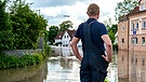 Ein Einsatzhelfer steht vor einer mit Hochwasser überfluteten Wohngegegend in Günzburg und sieht sich das Ausmaß an. | Bild: picture alliance / CHROMORANGE | Michael Bihlmayer