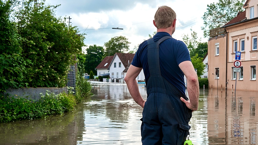 Ein Einsatzhelfer steht vor einer mit Hochwasser überfluteten Wohngegegend in Günzburg und sieht sich das Ausmaß an. | Bild: picture alliance / CHROMORANGE | Michael Bihlmayer