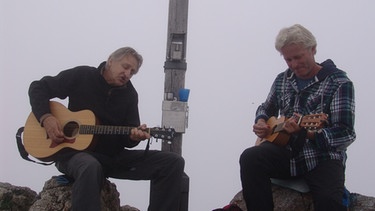 Werner Schmidbauer (rechts) und Kabarettist und Liedermacher Georg Ringsgwandl musizieren am Gipfelkreuz des 1720 Meter hohen Wildalpjoch im Sudelfeld. | Bild: BR/Werner Schmidbauer