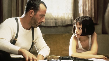 Léon (Jean Reno) betrachtet Mathilda (Natalie Portman) als eine Schülerin, der er den Umgang mit Waffen, nicht aber das Töten beibringt. | Bild: Studiocanal/Thierry Arbogast