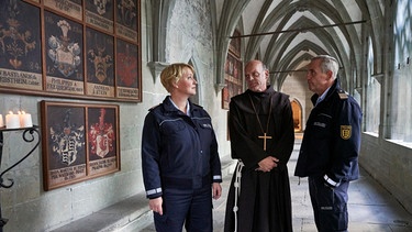 Paul Schott (Tim Wilde, rechts) und Nele Fehrenbach (Floriane Daniel, links) treffen Abt Barnabas (Ulrich Gebauer) im Kreuzgang von Kloster Oberzell. | Bild: ARD/Dominik Hatt