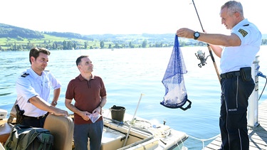 Jakob Frings (Max König, links) wartet gespannt auf die Erklärung des Schmuckhändlers Florian Arlen (Carsten Strauch, Mitte) zu dem Fund, den sein Kollege Paul Schott (Tim Wilde, rechts) soeben aus dem Wasser gefischt hat. | Bild: ARD/Laurent Trümper