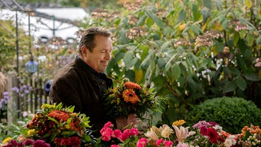 Beissl (Andreas Giebel) kauft seiner Frau einen Blumenstrauß. | Bild: ARD/Lucky Bird Pictures/Angela M. Schlabitz