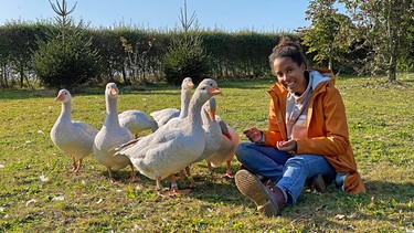 Alex’ Gänse sind so lieb, dass Pia sich schon nach kurzer Zeit zu ihnen setzen und mit ihnen um die Wette schnattern kann. | Bild: BR/Text und Bild Medienproduktion GmbH & Co. KG/Katharina Brackmann