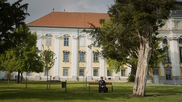 Johannes Holzinger auf einer Parkbank vor dem Kloster. | Bild: ORF/BR/Tellux-Film GmbH/Metafilm GmbH