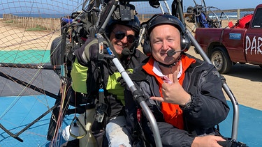 Ausflug von Valparaiso in Chile an den Strand von Concon. Gästebetreuer Bernd Wallisch (vorne im Bild) bereitet sich auf seinen Flug mit Pilot Gonzalo Lopez im Paratrike vor. | Bild: BR/Bewegte Zeiten Filmproduktion GmbH/Gerrit Mannes