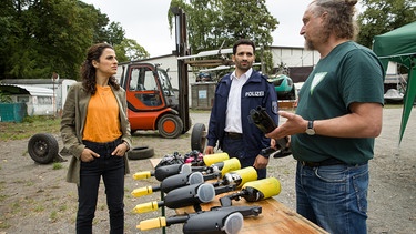 "Männerschutz"-Betreiber Uwe Brandis (Matthias Komm, rechts) behauptet gegenüber Jasmin Sayed (Sesede Terziyan, links) und Fahri Celik (Hassan Akkouch, Mitte), nur Sportwettbewerbe auszurichten. | Bild: ARD/Daniela Incoronato