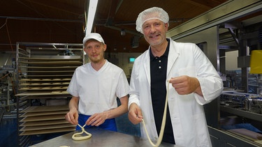 Von links: Franz Piller und Alexander Herrmann posieren beim Brezenteigschlingen in der Produktionsstätte der Bäckerei Piller in Karlsfeld. | Bild: BR/Jürgen Endriß