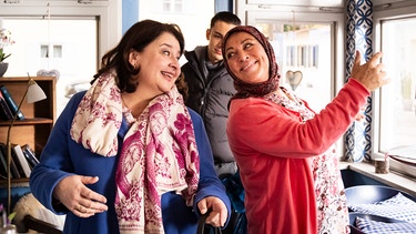 Monika und Sevim tanzen gemeinsam im Kiosk, während Leon am liebsten das Weite suchen würde. Von links: Monika (Christine Reimer), Sevim (Özay Aslanhan) und Leon (Joel Akgün). | Bild: BR/Lena Semmelroggen