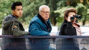 Hui (Aaron Le, links) und Günter (Peter Lerchbaumer, Mitte) beobachten das Café aus der Ferne. Hannah (Swetlana Schönfeld, rechts) benutzt einen Feldstecher. | Bild: ARD/Kai Schulz