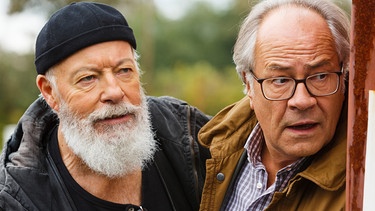 Reinhard Bielefelder (Bill Mockridge, links) und Klaus Schmitz (Hartmut Volle, rechts) beobachten aus einem Versteck heraus Naumann, der offensichtlich in Schwierigkeiten steckt. | Bild: ARD/Kai Schulz