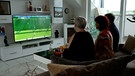 Drei Personen sitzen auf der Couch und schauen Fußball im Fernseher | Bild: BR