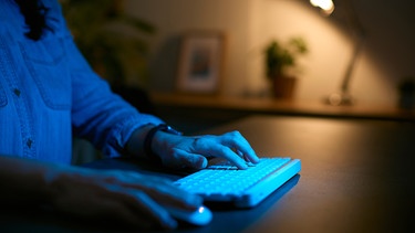 Eine Frau sitzt Abends vor dem Computer an ihrem Schreibtisch zuhause. | Bild: stock.adobe.com/Monkey Business