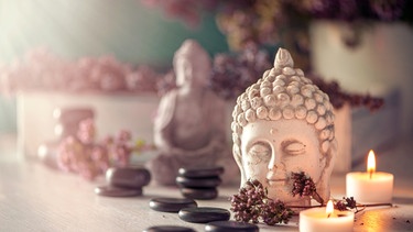 Steine für Hot Stone Massage, brennende Kerzen und ein Buddha. | Bild: stock.adobe.com/Sonja Birkelbach