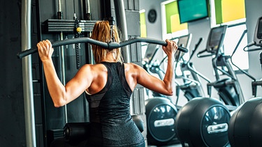 Eine Frau trainiert im Fitnessstudio ihre Rückenmuskulatur. | Bild: stock.adobe.com/insomniafoto