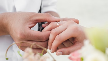 Der Bräutigam steckt der Braut bei der Hochzeit den Ring an. | Bild: stock.adobe.com/kostyazar