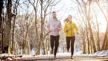 Ein junges Paar joggt auf einem winterlichen Waldweg. | Bild: stock.adobe.com/dusanpetkovic1