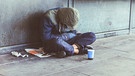 Ein Obdachloser sitzt am Boden auf dem Gehweg. | Bild: stock.adobe.com/FollowTheFlow