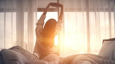 Eine junge Frau streckt sich früh morgens in Bett.  | Bild: stock.adobe.com/oatawa