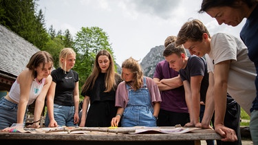 Schülerinnen stehen im Freien um einen Tisch mit Papier herum  | Bild: Florian Breitenberger