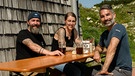 Von links: Die Pächter des Stöhrhauses, Florian Freundl und Karina Rommel, mit Marcus Fahn auf der Terrasse. | Bild: BR/Watch Lola GmbH/Matthias Schwinn