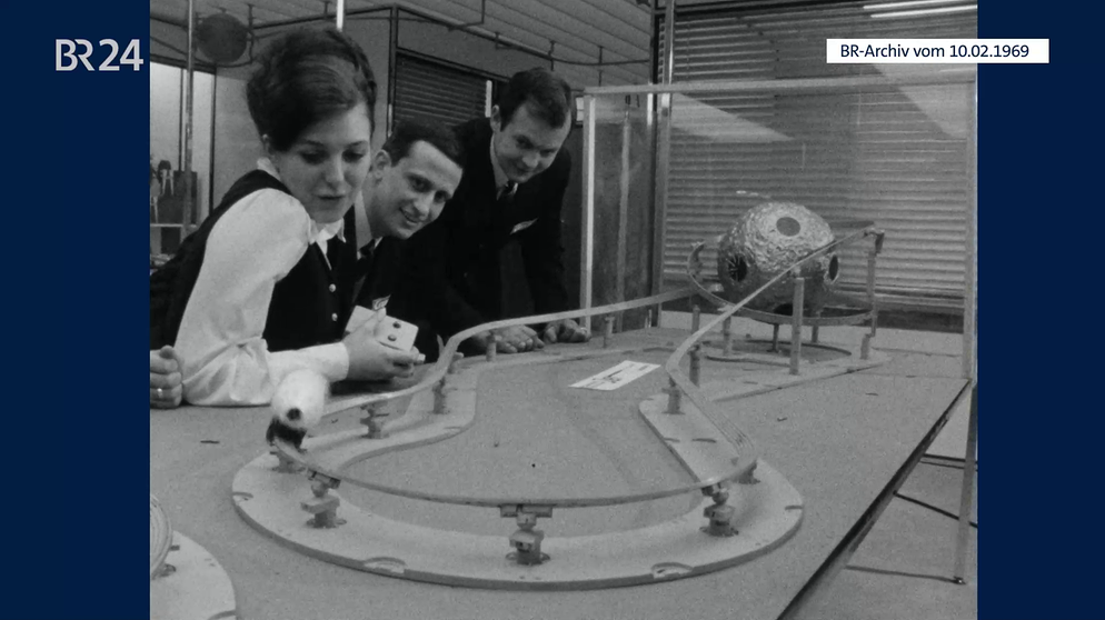 Frau beim Spielen mit der Rennbahn Carrera Jet Apollo. Zwei Männer sehen ihr dabei zu. | Bild: BR-Archiv