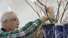 Ein Mann mit weißen Haaren steckt einen Blumenstrauß | Bild: BR 