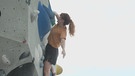 Eine kletternde Frau, welche in einer Boulderhalle trainiert. Sie hält sich nur mit einer Hand fest. | Bild: BR