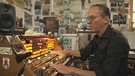 Der Münchener Peter Pichler sitzt und spielt ein einzigartiges Instrument, das Trautonium. In einem Zimmer voller Elektronik | Bild: BR