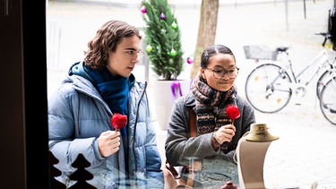 Dahoam is Dahoam: Lien (Nui Nguyen) steht mit Till (Marinus Hohmann) vor einem Schaufenster und versucht subtil ihm einen Tipp zu geben, was ihr gefällt. | Bild: BR/Lena Semmelroggen