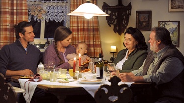 Dahoam is Dahoam: Julian und Sophia sitzen gemeinsam mit Lenz, Stadlbauer und Monika am Weihnachtstisch. Von links: Julian (Sandro Kirtzel), Sophia (Patricia Freund), Monika (Christine Reimer), Stadlbauer (Andreas Geiss). | Bild: BR/Marco Orlando Pichler