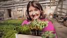 Dahoam is Dahoam: Moni (Christine Reimer) hält einen Blumenkasten in der Hand, der mit Tomaten, Erdbeeren und Kräutern bepflanzt wurde. | Bild: BR/Markus Walsch