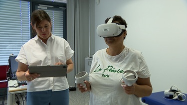 Eine Patientin mit einer VR-Brille (rechts) steht neben einer Frau im Uniklinikum Erlangen | Bild: BR