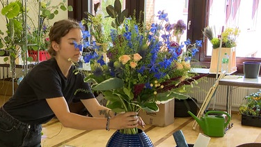 Frau stellt Blumenstrauß in die Vase. | Bild: BR