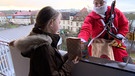 Ein als Nikolaus verkleideter Höhenretter beschenkt ein Kind am Balkon. | Bild: BR