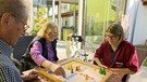 Eine Pflegerin spielt mit zwei Senioren ein Brettspiel. | Bild: BR