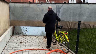 Uwe Heyder mit Rad vor Mauer. | Bild: BR