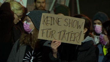 Eine Protestierende hält ein Schild mit der Aufschrift "Keine Show für Täter" hoch. | Bild: BR