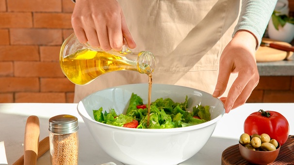 Frau bereitet einen Salat mit Olivenöl zu. | Bild: mauritius images / Pixel-shot / Alamy / Alamy Stock Photos