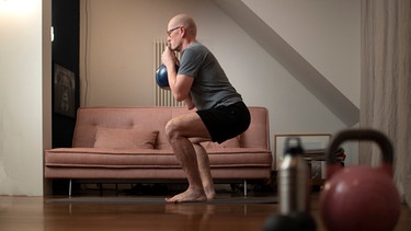 Ein Mann macht eine Kniebeuge mit Gewichten. | Bild: picture-alliance/dpa