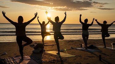 dpatopbilder - 21.06.2023, Großbritannien, Scarborough: Mitglieder der Happy Seal Yoga-Klasse üben an der Cayton Bay, während die Sonne zur Feier der Sommersonnenwende aufgeht. Foto: Danny Lawson/PA Wire/dpa +++ dpa-Bildfunk +++ | Bild: dpa-Bildfunk/Danny Lawson